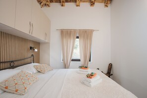 Un dormitorio con una cama, cabecera de madera, ventana con cortinas y mesita de noche con lámpara.
