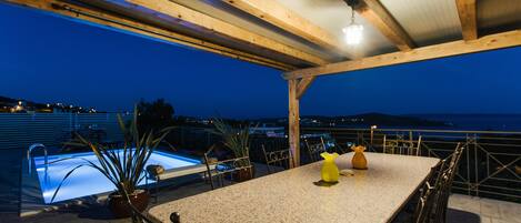An outdoor pool area with a table and chairs, surrounded by a wooden pergola structure.