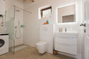 Un bagno con doccia vetro, un water, una lavatrice e un lavandino con specchio.