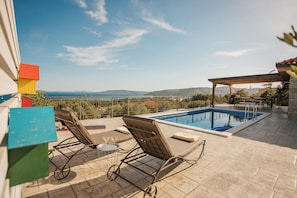 A rooftop pool area with lounge chairs, a pergola, and a view of the sea.
