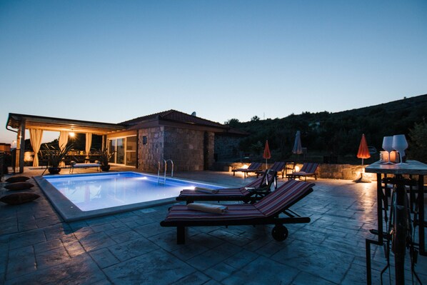 Area piscina con lettini e ombrelloni, una zona relax coperta e un edificio in pietra.