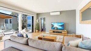 Ein modernes Wohnzimmer mit großem Fernseher, bequemen Sitzgelegenheiten und Blick ins Freie.