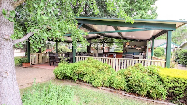 En udendørs patio med overdækket siddeområde, en bar og et ur på væggen.