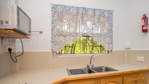 A kitchen with a stainless steel sink, wooden cabinets, a microwave, and a window with a floral curtain.