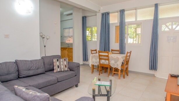 A living room with a grey sofa, a glass coffee table, and a dining area with wooden chairs and a table.