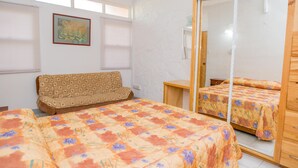A bedroom with two beds, a sofa, a large mirror, and a window with blinds.