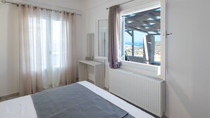 A bedroom with a bed, a window with curtains, a radiator, and a view of the outside. - Villa Thetis with private pool and sea view (Paros)