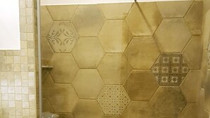 Ein Badezimmer mit sechseckisch gemusterten Fliesen, einer Duschkabine aus Glas und einem weißen Waschbecken.