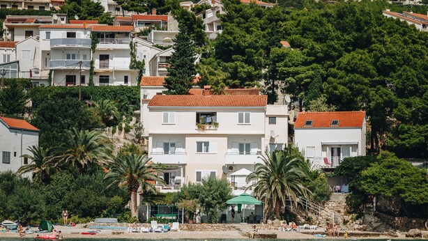 Un edificio costero con balcones, una playa en primer plano y abundante vegetación.