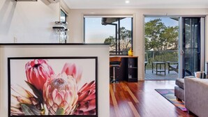 A modern living room with a large framed floral artwork, a wooden floor, a sofa, and a sliding glass door leading to an outdoor area with a table and chairs.