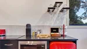 A kitchen with a stainless steel oven, a red refrigerator, and a window with a view of trees.