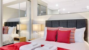 A modern hotel room with a large bed, red and white bedding, a mirror, and a nightstand with a lamp.