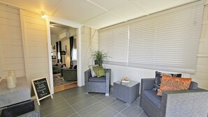 Een moderne woonkamer met grijze banken, een salontafel en een potplant. Links een bord met krijt en rechts een raam met jaloezieën.