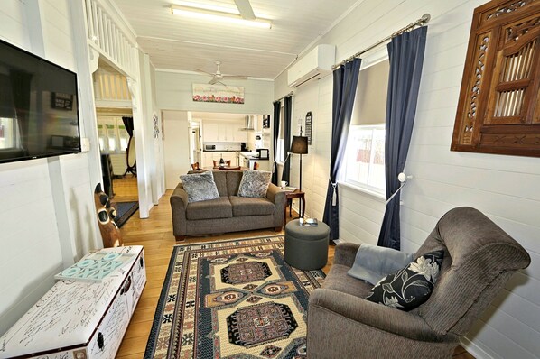 A cozy living room with a sofa, ottoman, and a coffee table. A kitchen is visible in the background.
