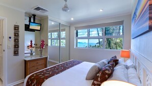 A bedroom with a large bed, a dresser, a mirror, and a window with a view of the sea.