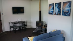 Een woonkamer met een blauwe bank, een aan de muur bevestigde televisie, een open haard en drie abstracte schilderijen.