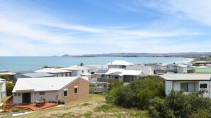 Un quartier résidentiel situé sur la côte, avec des maisons modernes, dont certaines sont équipées de panneaux solaires, et qui offre une vue sur la mer et les collines lointaines.