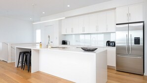 Une cuisine moderne avec des meubles blancs, un réfrigérateur en acier inoxydable et un îlot central doté de tabourets.