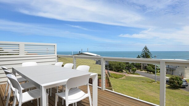 Une terrasse avec une table et des chaises, donnant sur un espace verdoyant et la mer.