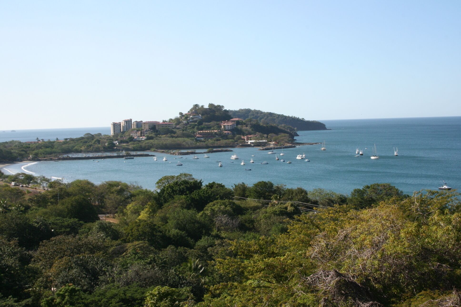 Une ville côtière avec des bâtiments situés sur une colline surplombant la mer, entourée d’une végétation luxuriante.
