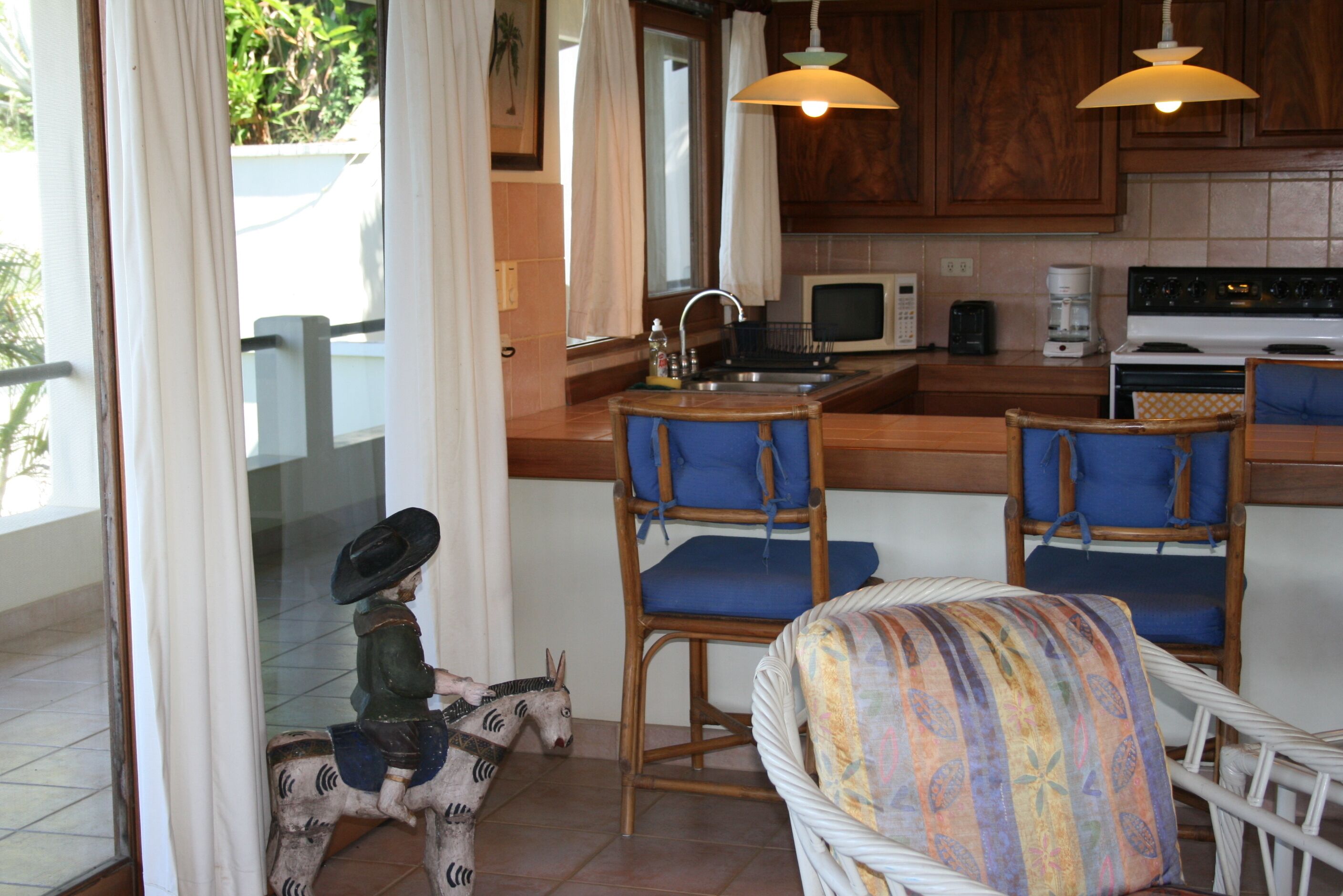 A kitchen with wooden cabinets, a microwave, a stove, and two bar stools with blue cushions.