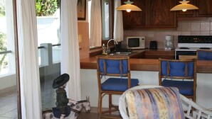A kitchen with wooden cabinets, a microwave, a stove, and two bar stools with blue cushions. - Stunning Villas, Ocean Views Plus a Pool - VILLAS CASA LOMA - Villa 2 (Playa Flamingo)