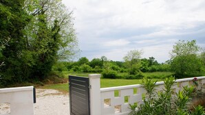 A gated entrance with a white fence and a black gate, surrounded by lush greenery and trees. - Holiday apartment in village Dobrani (Dobrani)
