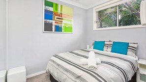 Relax in a serene space with a neatly made bed, lush views, and a vibrant art piece.
