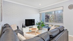 Relax in this stylish living room with a large flat-screen TV, comfortable sofa, and a view of the outdoors.