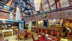 Ein Restaurant mit Holztischen, einer Bar und einem Strohdach.