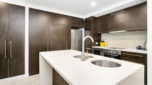 Een moderne keuken met donkerhouten kastjes, roestvrijstalen apparatuur en een wit aanrecht.