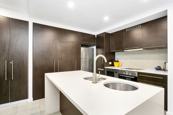 Una cocina moderna con armarios de madera oscura, electrodomésticos de acero inoxidable y encimera blanca.