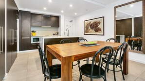 Een moderne keuken met donkere kasten, een wit aanrechtblad en een eetgedeelte met een houten tafel en zwarte stoelen.
