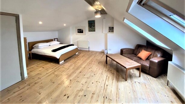 Ein Schlafzimmer mit Bett, Holzboden, einer Couch und einem Tisch.