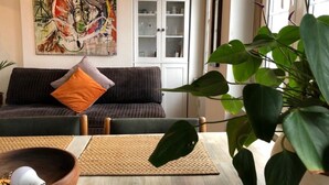 Ein Wohnzimmer mit einer Couch, Kissen, einem Schrank und einer großen Pflanze.