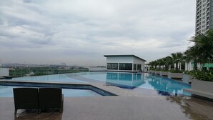 Une piscine sur le toit offrant une vue sur les gratte-ciel de la ville, un petit bâtiment et des palmiers.