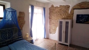 Une chambre avec un lit, une armoire, une fenêtre avec des rideaux et un mur en briques apparentes.