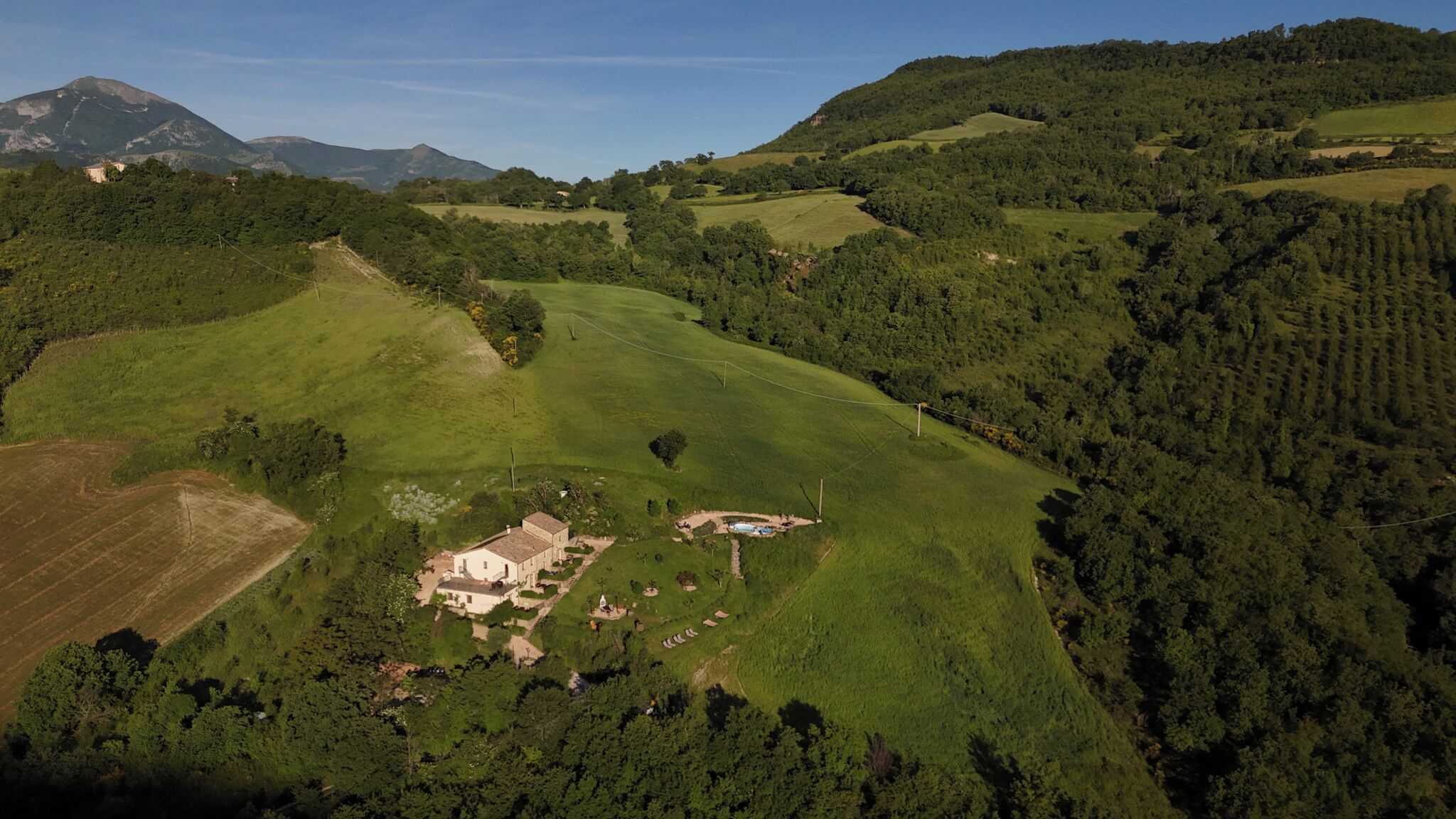 A rural landscape with rolling hills, a small building with a pool, and dense forest areas.