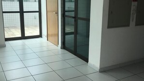 A clean, modern hallway with tiled flooring, a glass door, and a wooden door leading to a balcony. - studio golden breeze 1101 (recife)