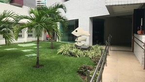 A courtyard with palm trees, a sculpture, and a building with white tiled walls. - studio golden breeze 1101 (recife)