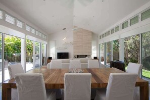 Un comedor moderno con una gran mesa de madera, sillas blancas, un televisor de pantalla plana y una chimenea de piedra.