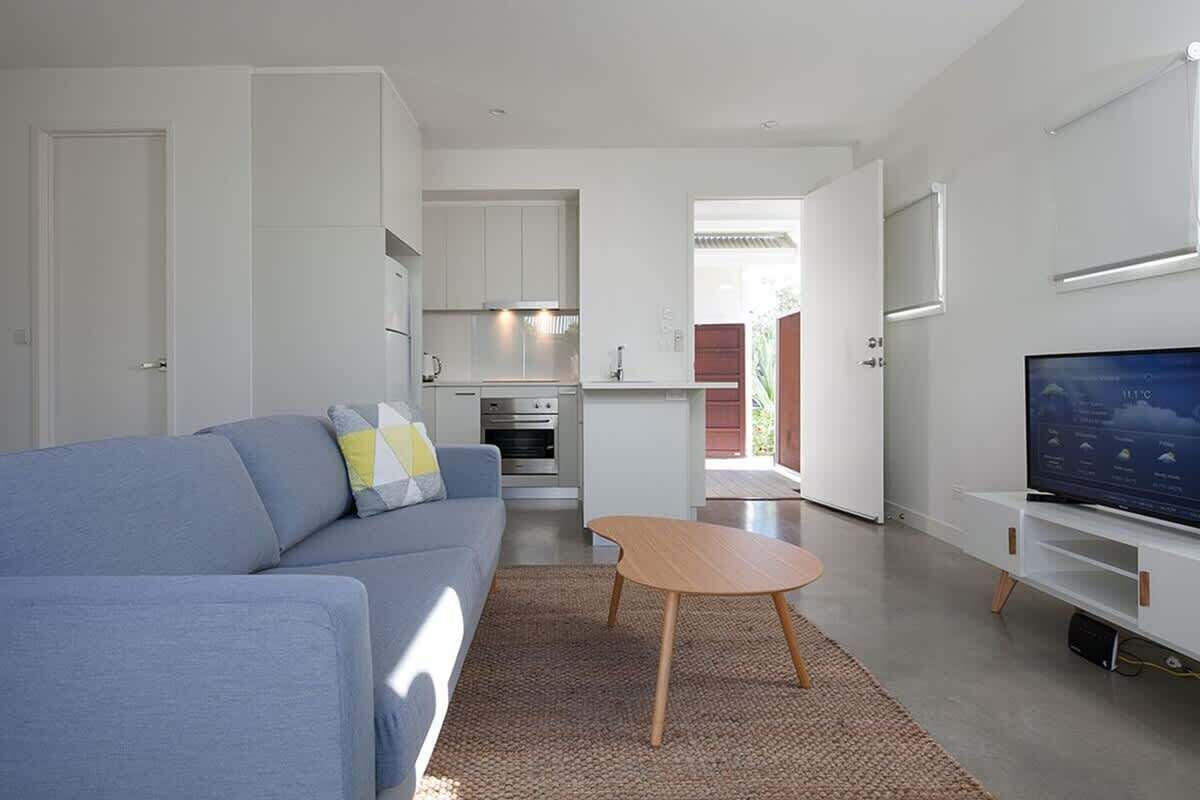 A modern living room with a sofa, a coffee table, a TV, and a kitchen area.