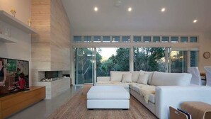 A modern living room with a sectional sofa, a flat-screen TV, and a fireplace. - White Sands Beach House (Marcoola)