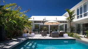 A modern pool area with a clear blue pool, lounge chairs, and a covered seating area. - White Sands Beach House (Marcoola)