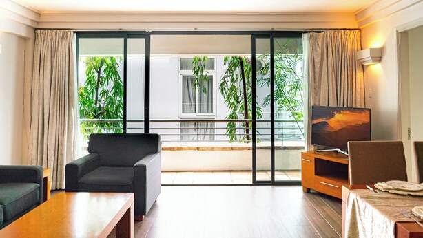 A modern living room with a sofa, a coffee table, a TV on a wooden stand, and a balcony with plants.