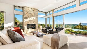 A modern living room with a stone fireplace, large windows, and a view of a mountainous landscape. - The Springs - architect-designed home with pool (Wilsons Creek)