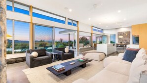A modern living room with large windows, a sofa, a coffee table, and a dining area. - The Springs - architect-designed home with pool (Wilsons Creek)