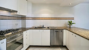 Een moderne keuken met witte kasten, een granieten aanrechtblad, roestvrijstalen apparatuur en inbouwspots.