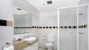 Een moderne badkamer met een wit wastafelmeubel, een beige blad, een toilet en een douche met glazen wanden.