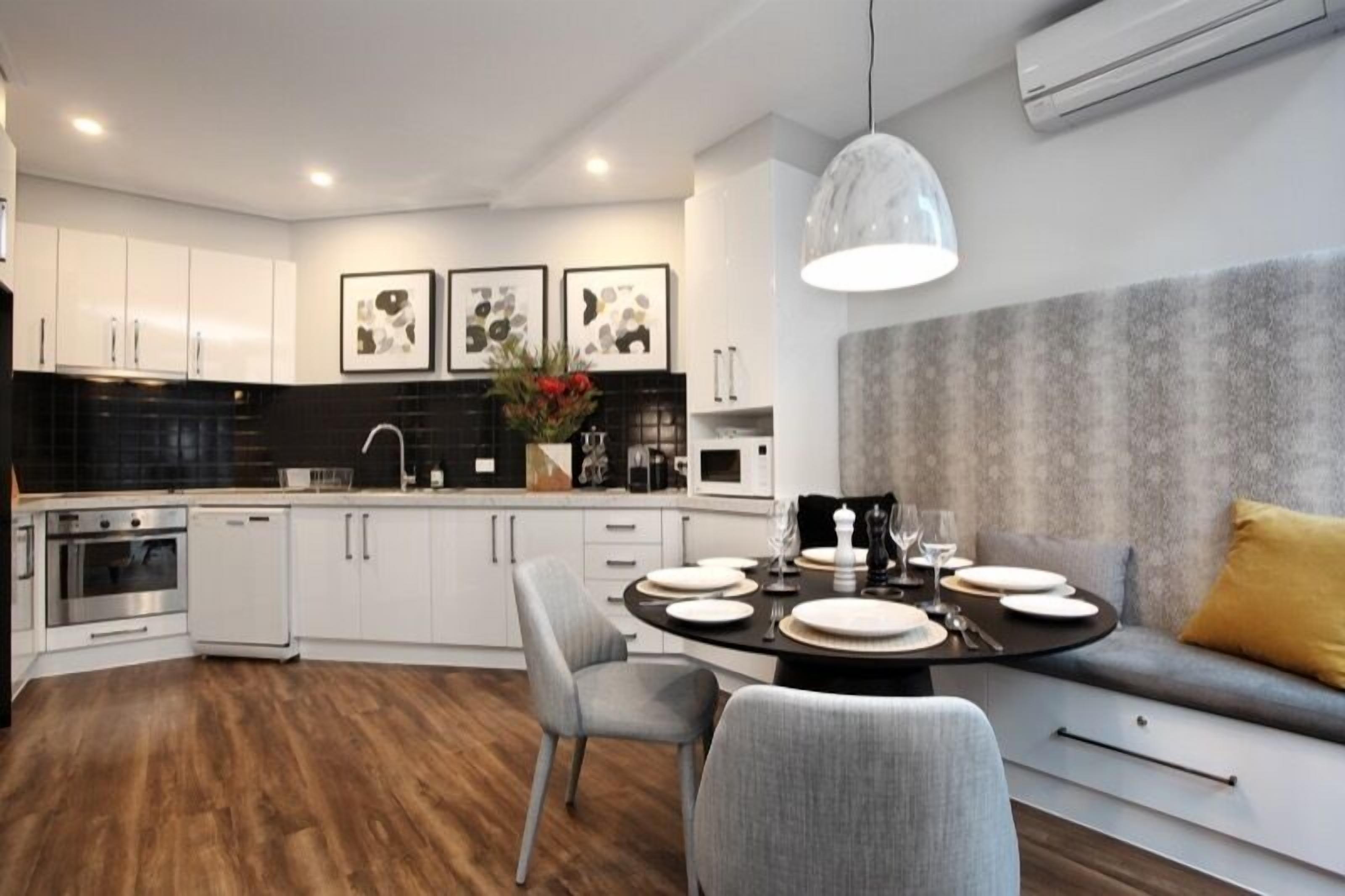A modern kitchen with white cabinets, a black backsplash, and a dining area with a round table set for four.